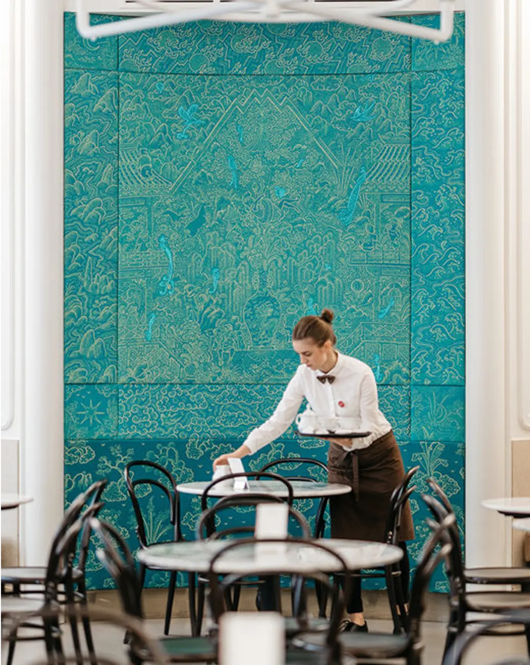 Waitress preparing tables in the interior of Myšák pastry shop.
