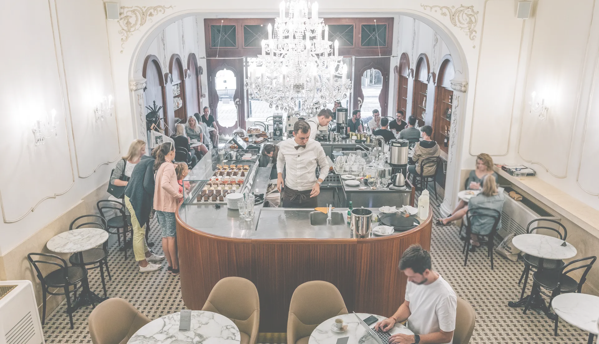 Interior of Myšák patisserie with central counter and guests.